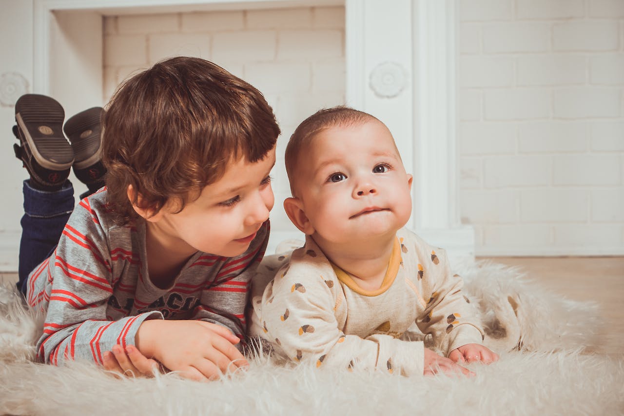 Two adorable siblings enjoy a moment of togetherness on a fluffy rug, exuding innocence and love.